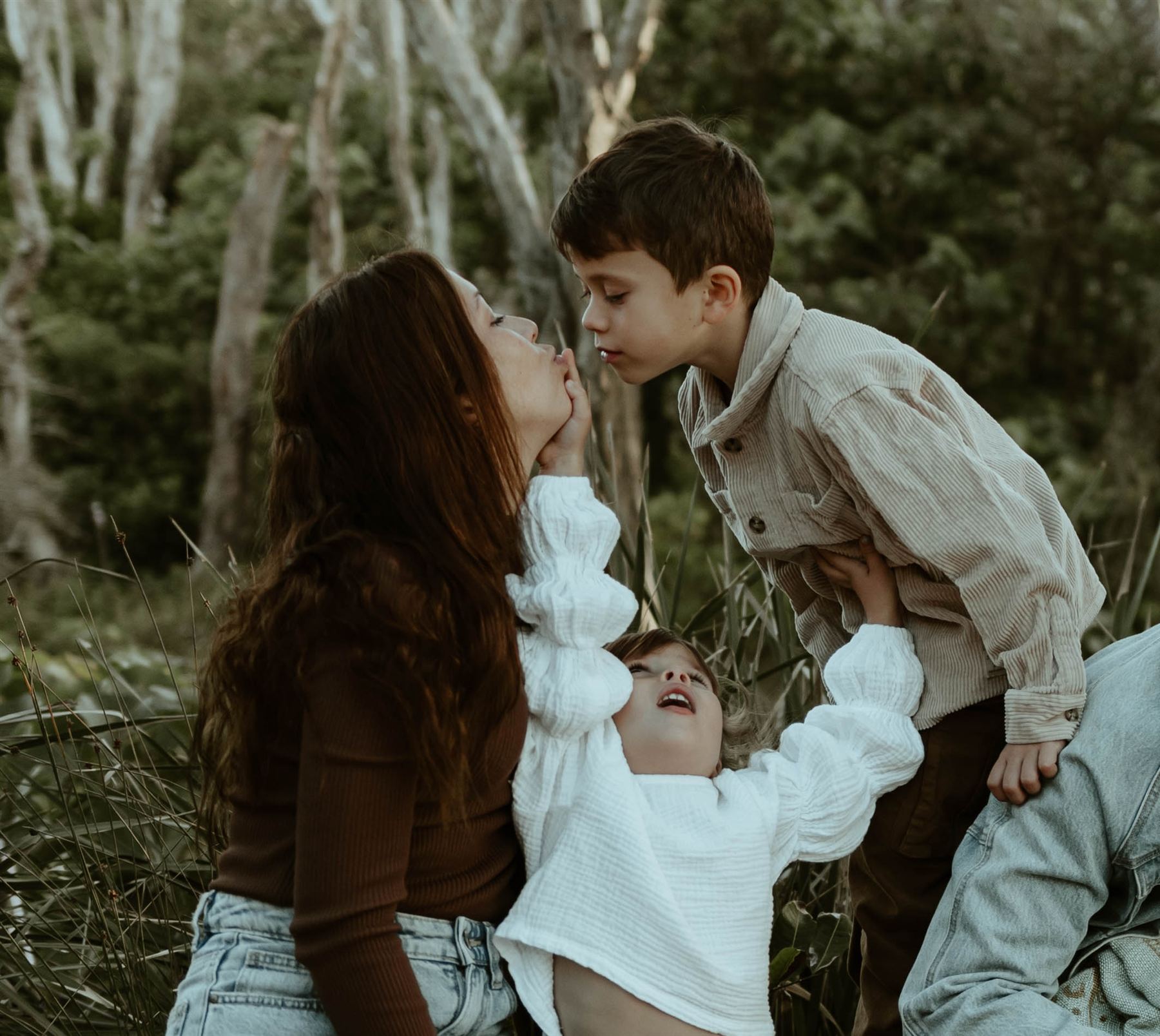 Mother being kissed by her son while her toddler plays in her lap