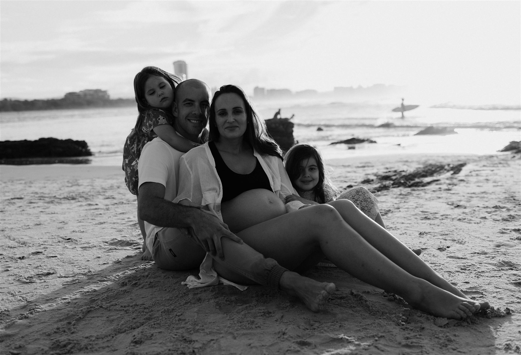 Black and white photograph of a family sitting together on the sand at sunset
