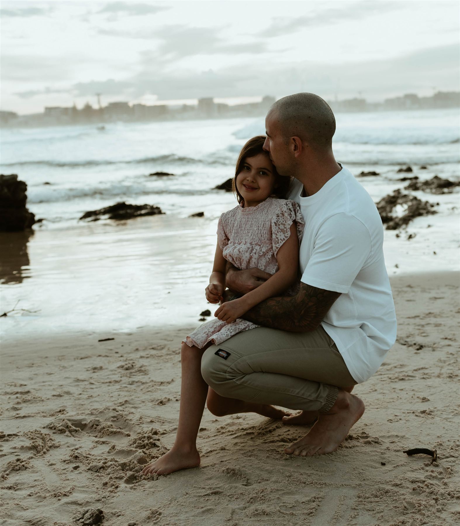 Father kissing his daughter's head on the beach at dusk