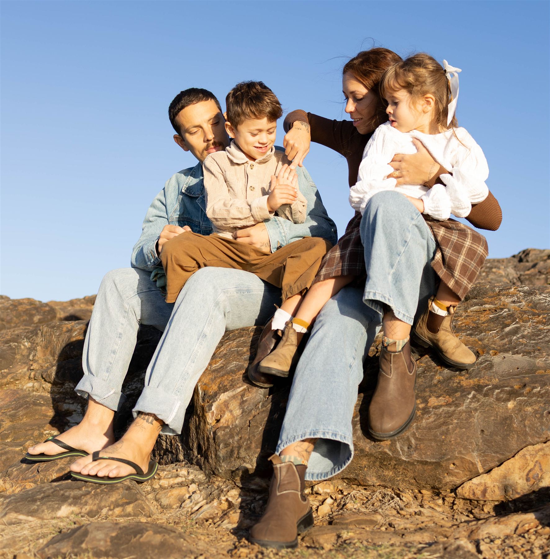 Family of four sitting together on golden rocks under a clear blue sky