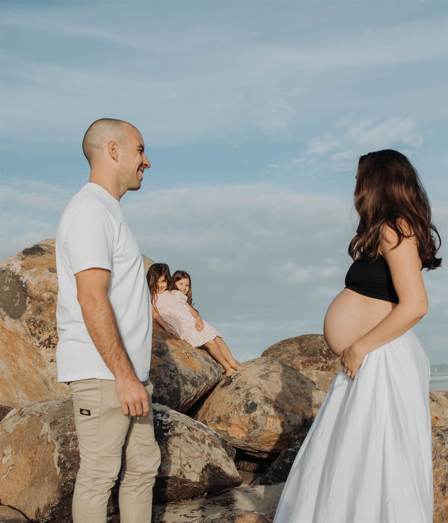 Expecting couple standing among beach rocks in soft morning light